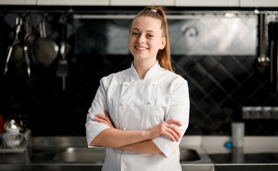 a smiling woman in a chef's coat in a clean commercial kitchen